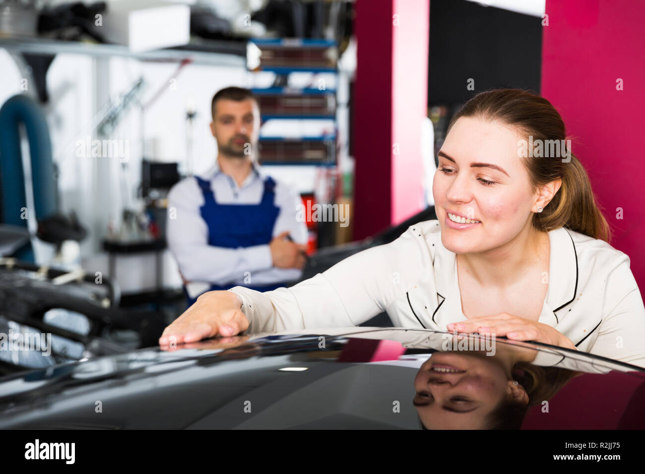 Smiling elegant woman admiring her car after repainting at auto service Stock Photo
