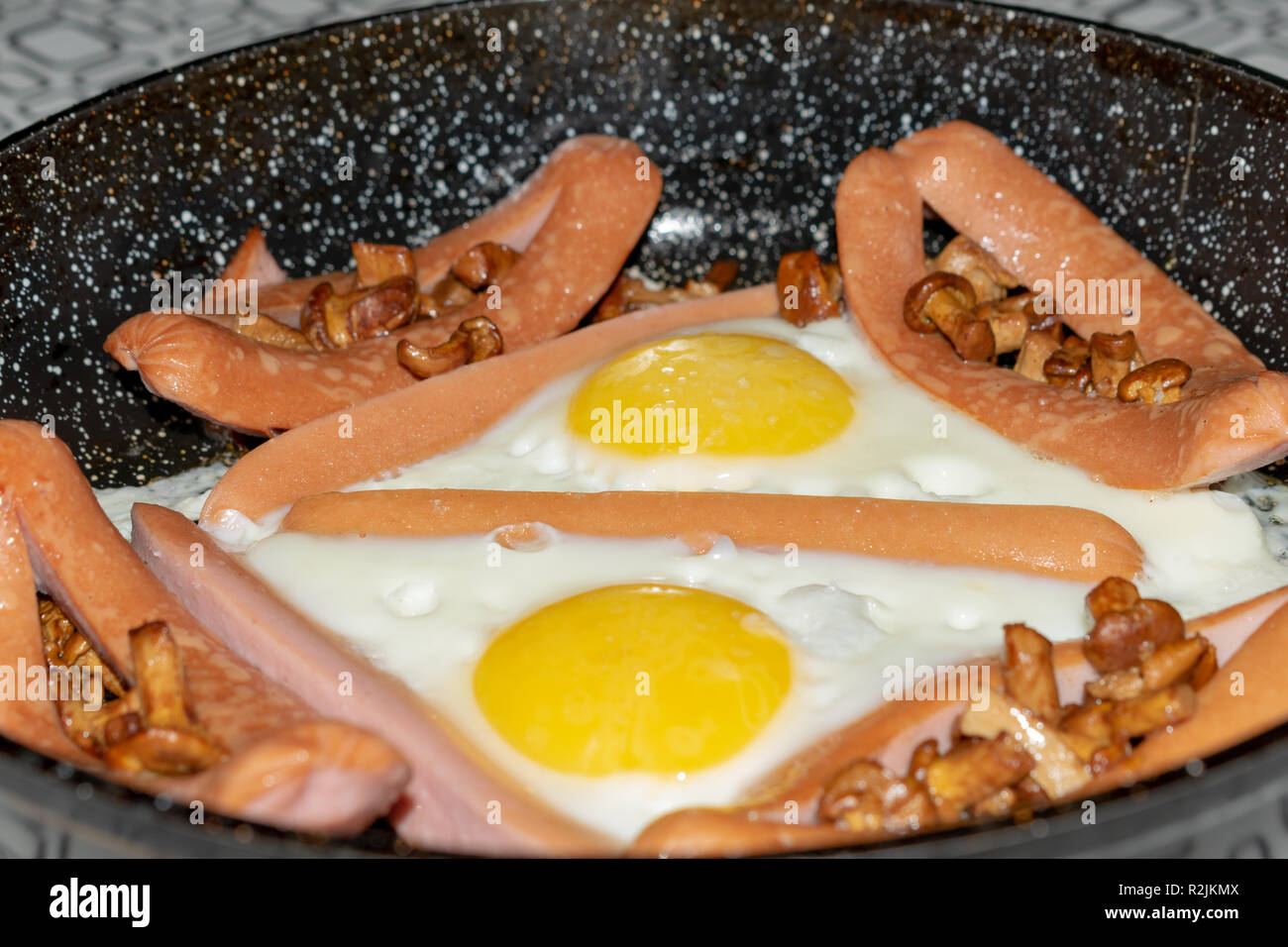 Cast iron pan with fried eggs, sausage, mushrooms and beans on a wooden table. Top view, delicious food. Stock Photo