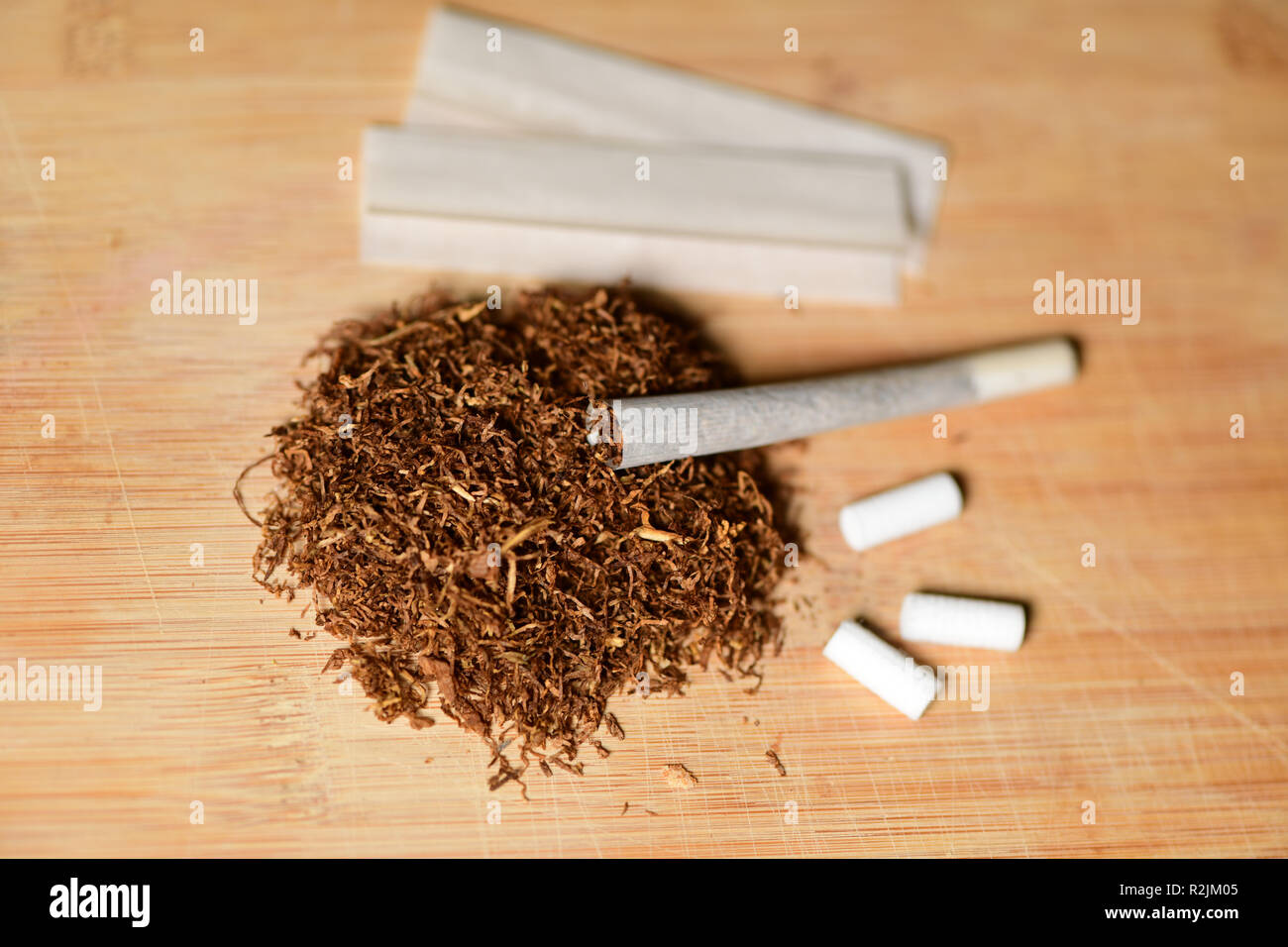 Hand rolling tobacco, paper and filters to make cigarettes on rustic