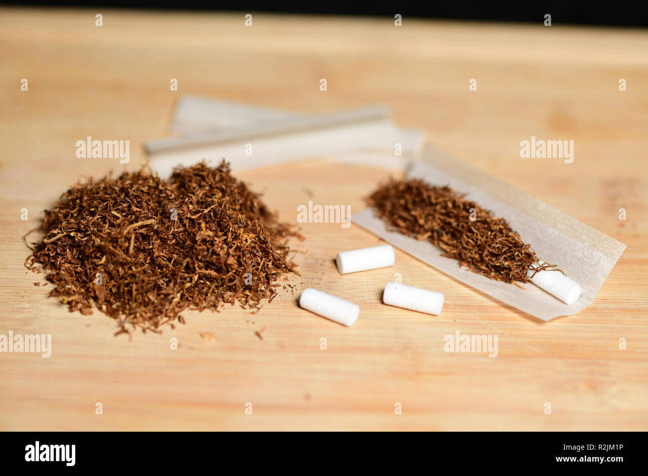 Hand rolling tobacco, paper and filters to make cigarettes on rustic wood  Stock Photo - Alamy