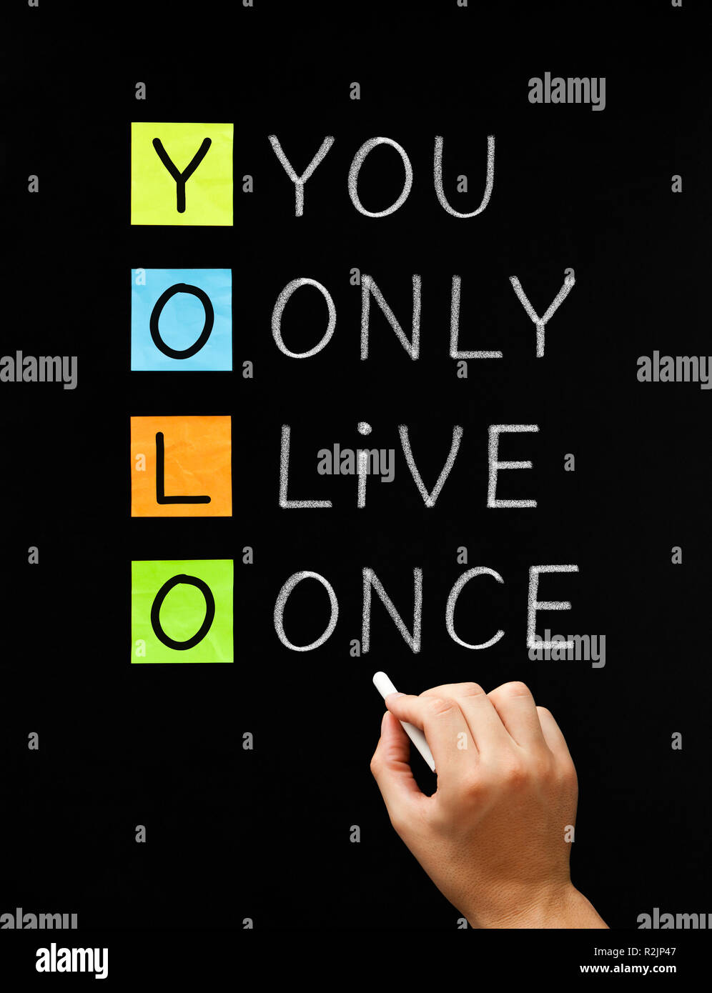 Hand writing the motto acronym YOLO - You Only Live Once with white chalk on blackboard. Stock Photo