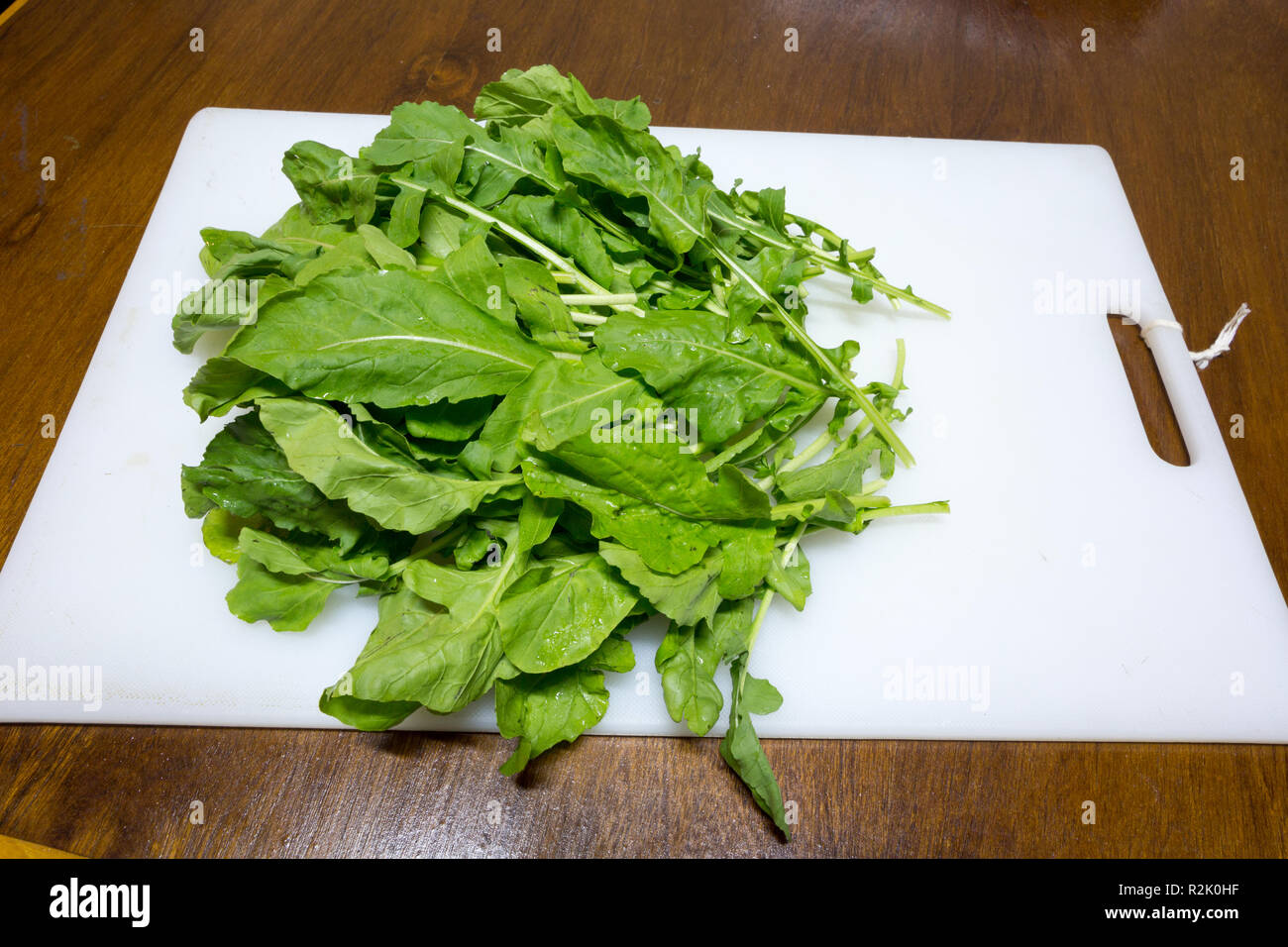 Arugula or rocket (Eruca sativa; syns. Eruca vesicaria) leaf vegetable on white cutting board, Asuncion, Paraguay Stock Photo