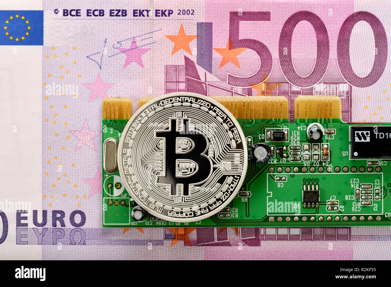 Symbolic image of digital currency, silver physical coin Bitcoin on 500 EURO banknote and circuit board Stock Photo