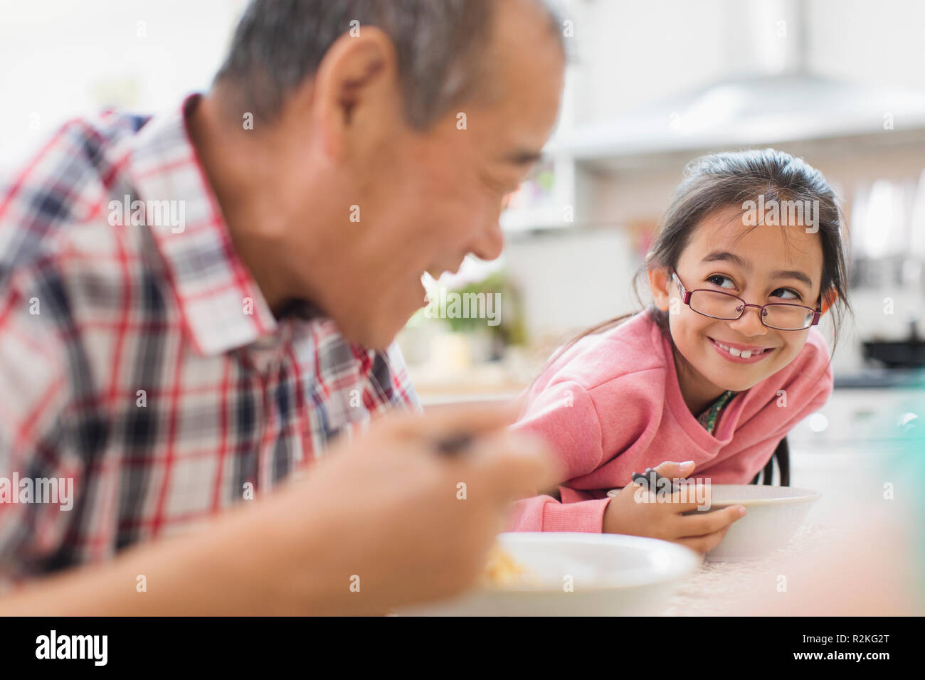 Smiling grandfather and granddaughter eating at table Stock Photo