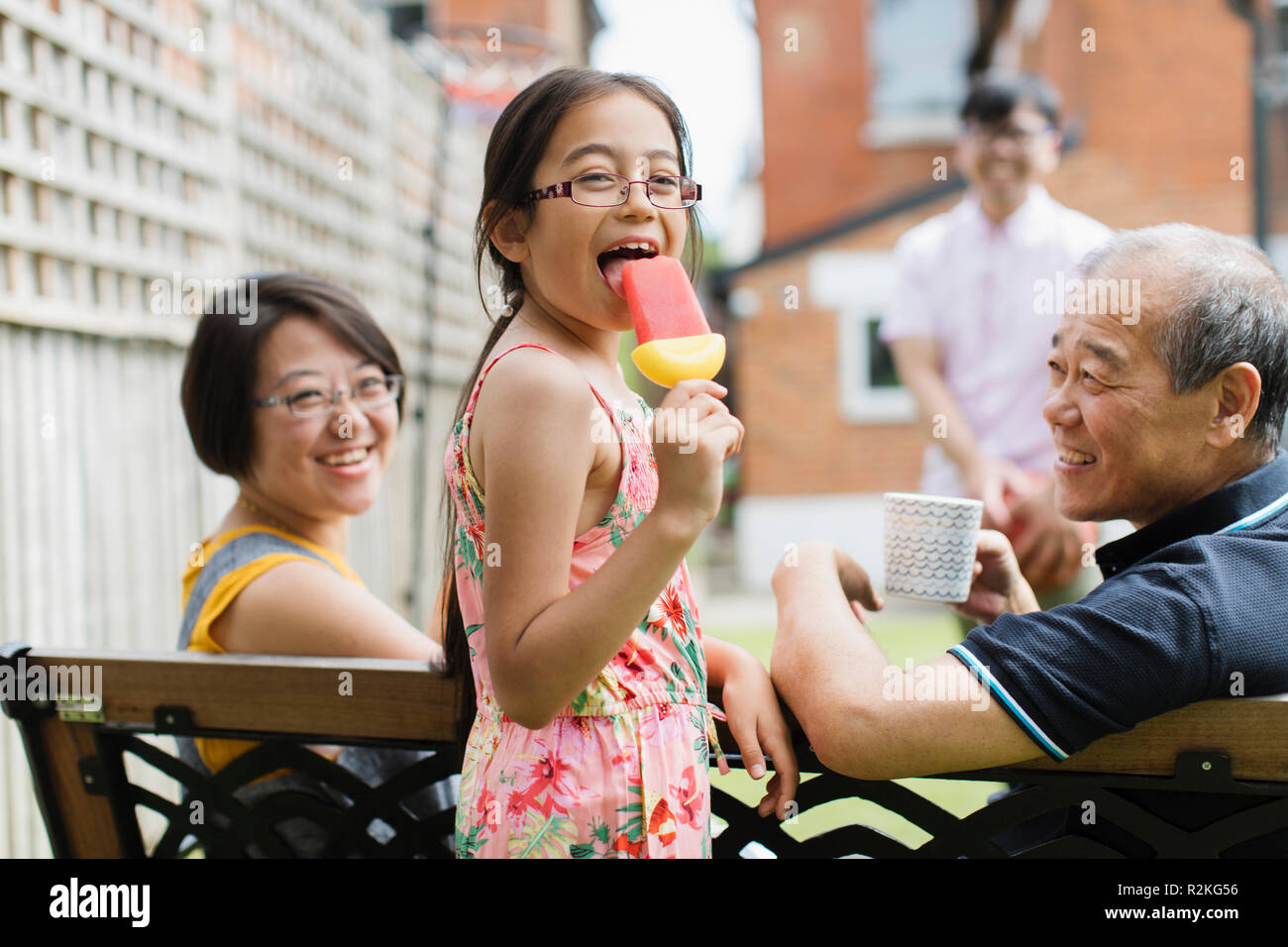 Portrait happy girl eating flavored ice with multi-generation family in back yard Stock Photo