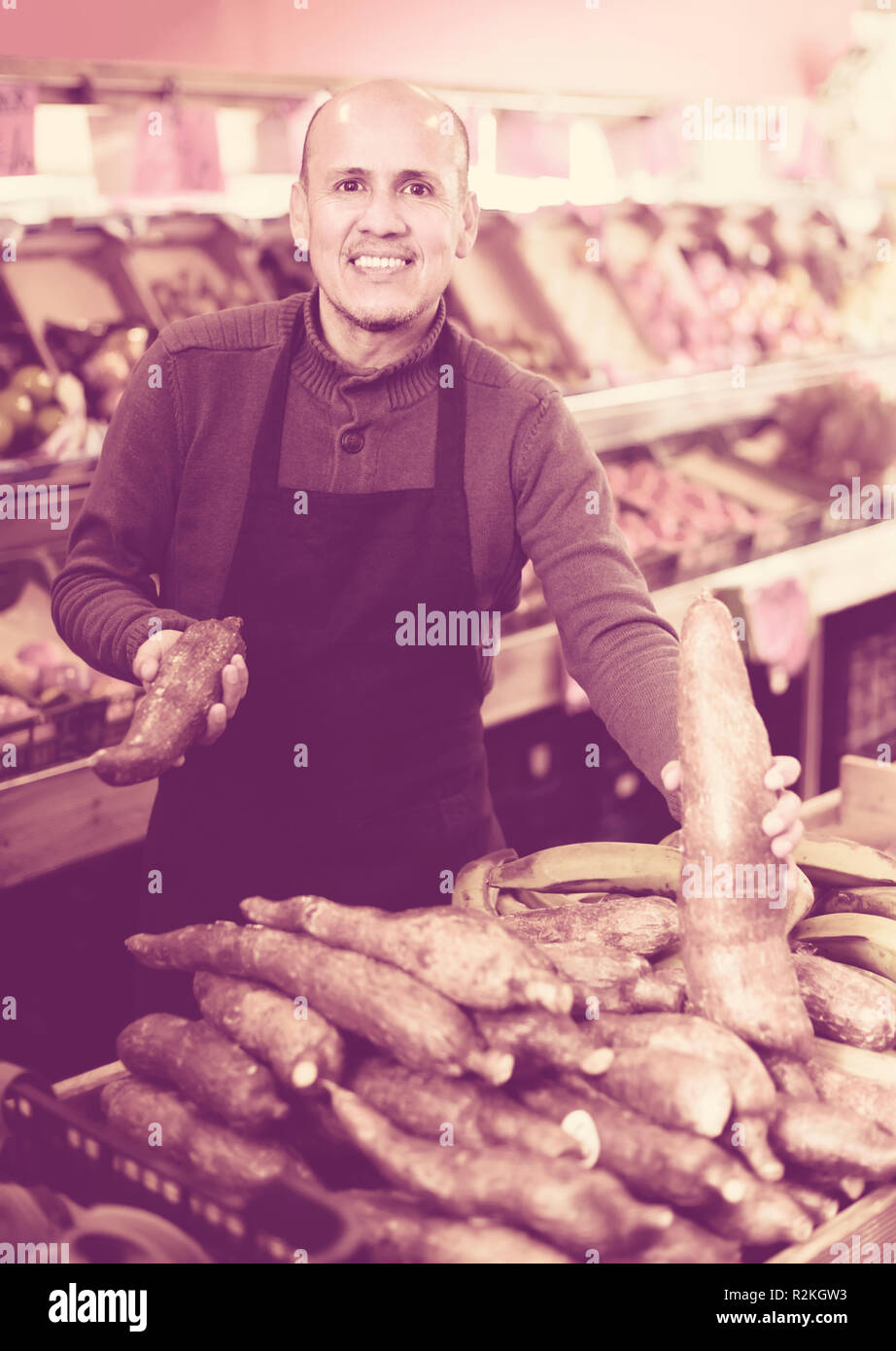 Smiling senior worker selling ripe cassava roots in supermarket Stock Photo