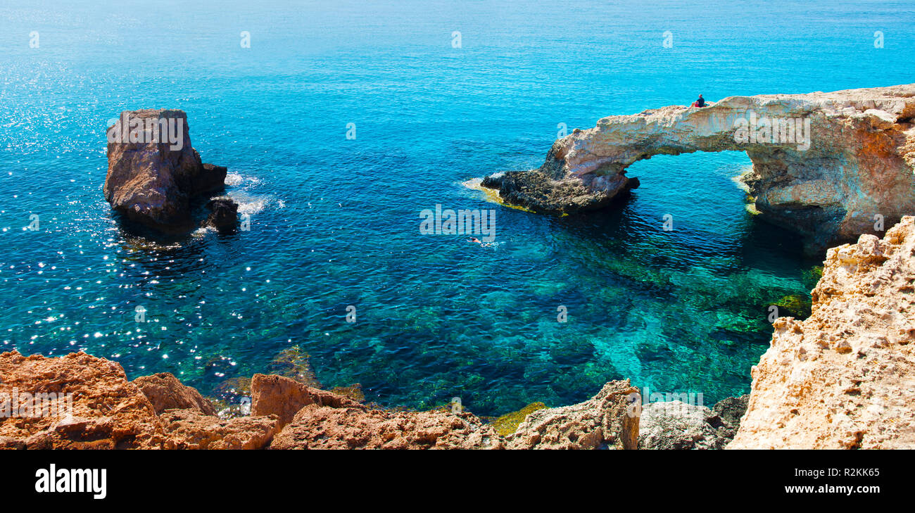 One man sitting on a natural landmark Love Bridge. Panoramic view of yellow stone cliffs near transparent crystal clear amazing green water. Warm clou Stock Photo