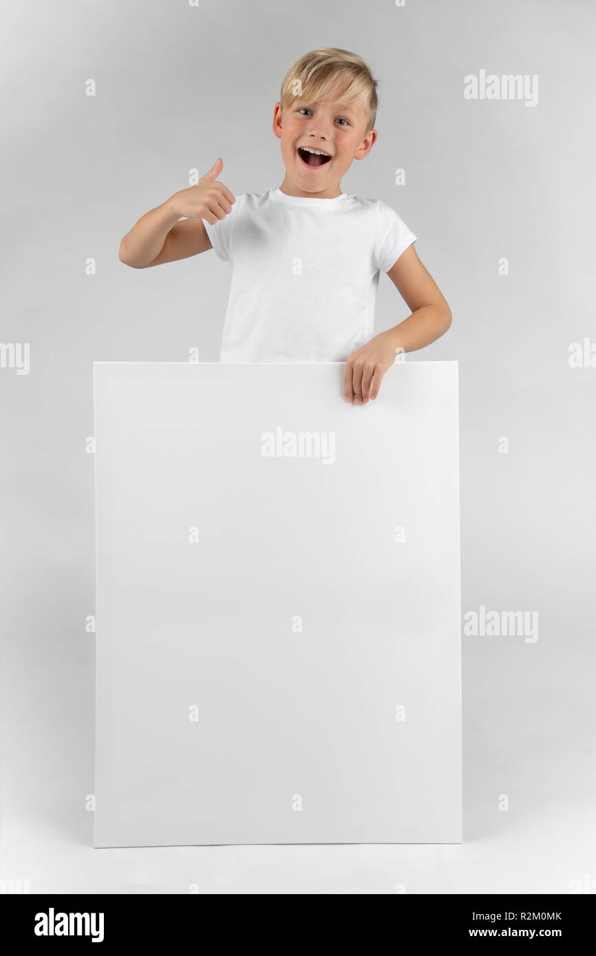 little blond boy holds a blank sign in his hands and points with his thumb upwards. Stock Photo