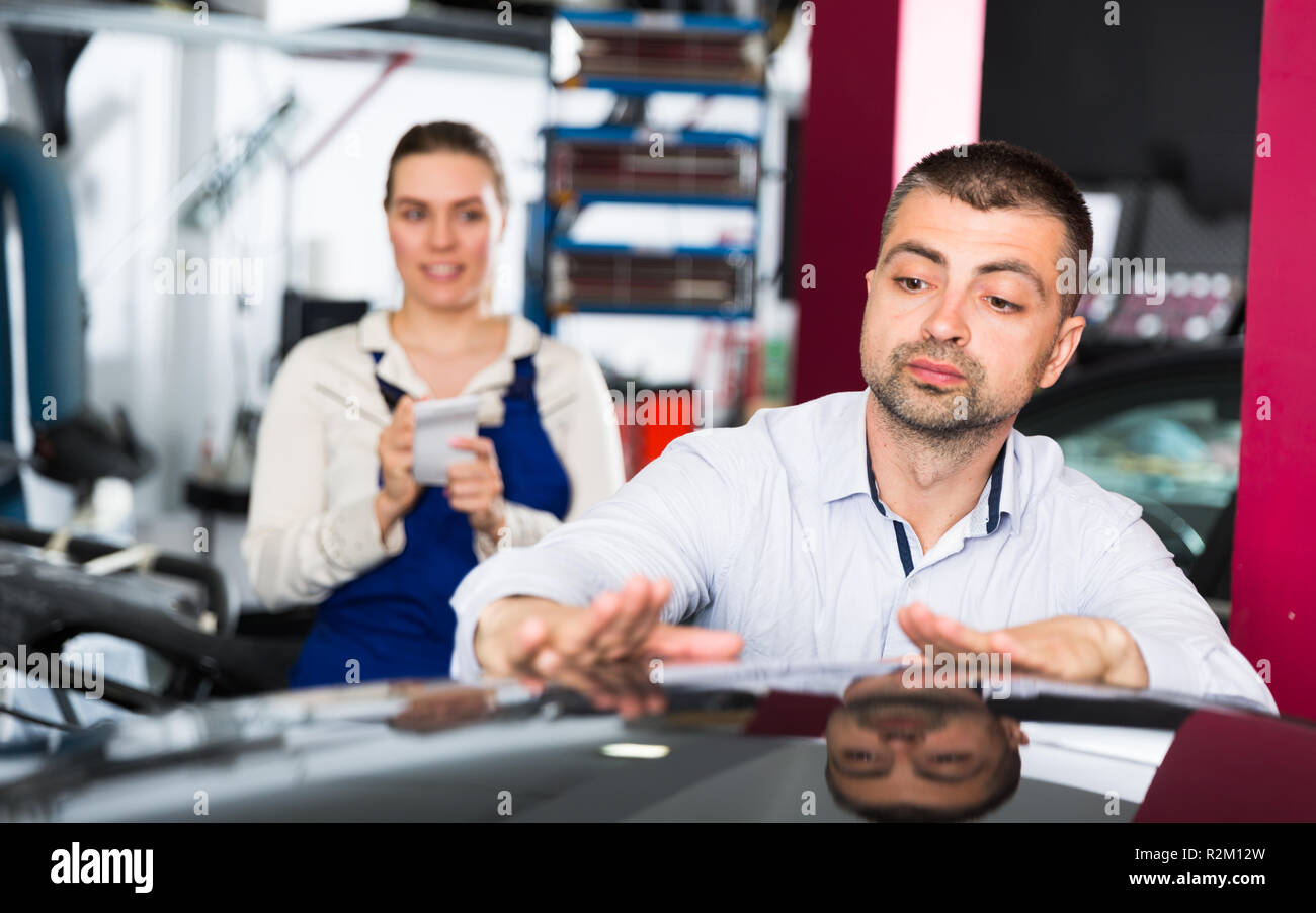 Concentrated male car owner touching surface repainted body, checking painting quality in car repair shop Stock Photo