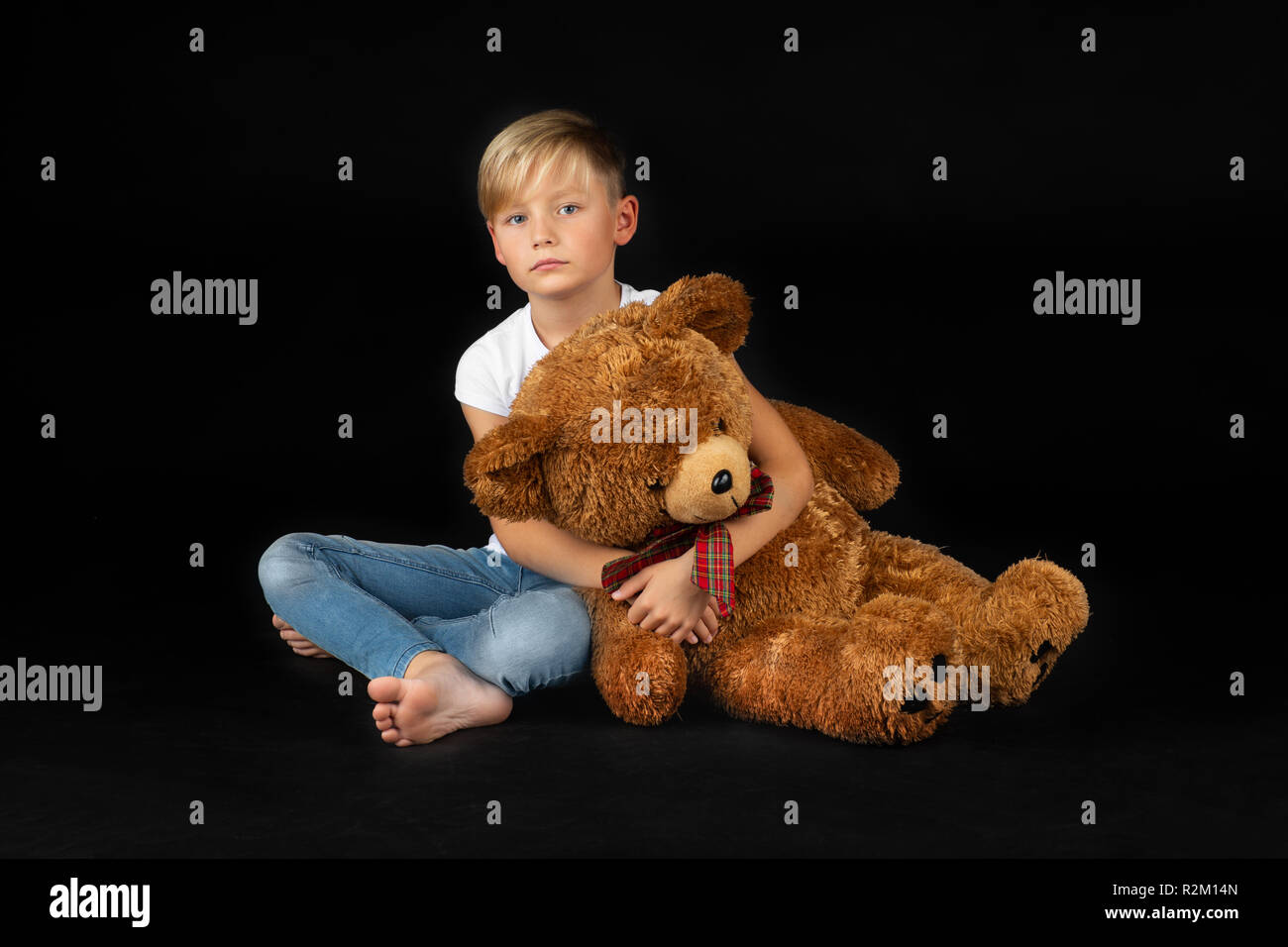 little blond boy is sitting sadly on the floor with a big teddy bear ...