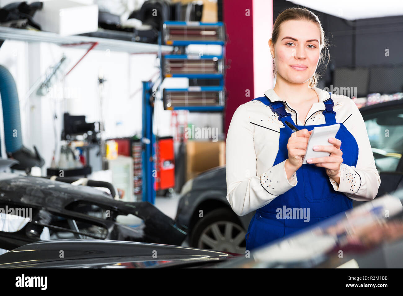 Smiling girl auto mechanic taking notes on notebook in car painting workshop Stock Photo