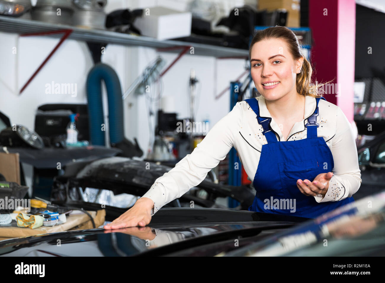 Young woman mechanic demonstrating repainted car in auto repair shop Stock Photo