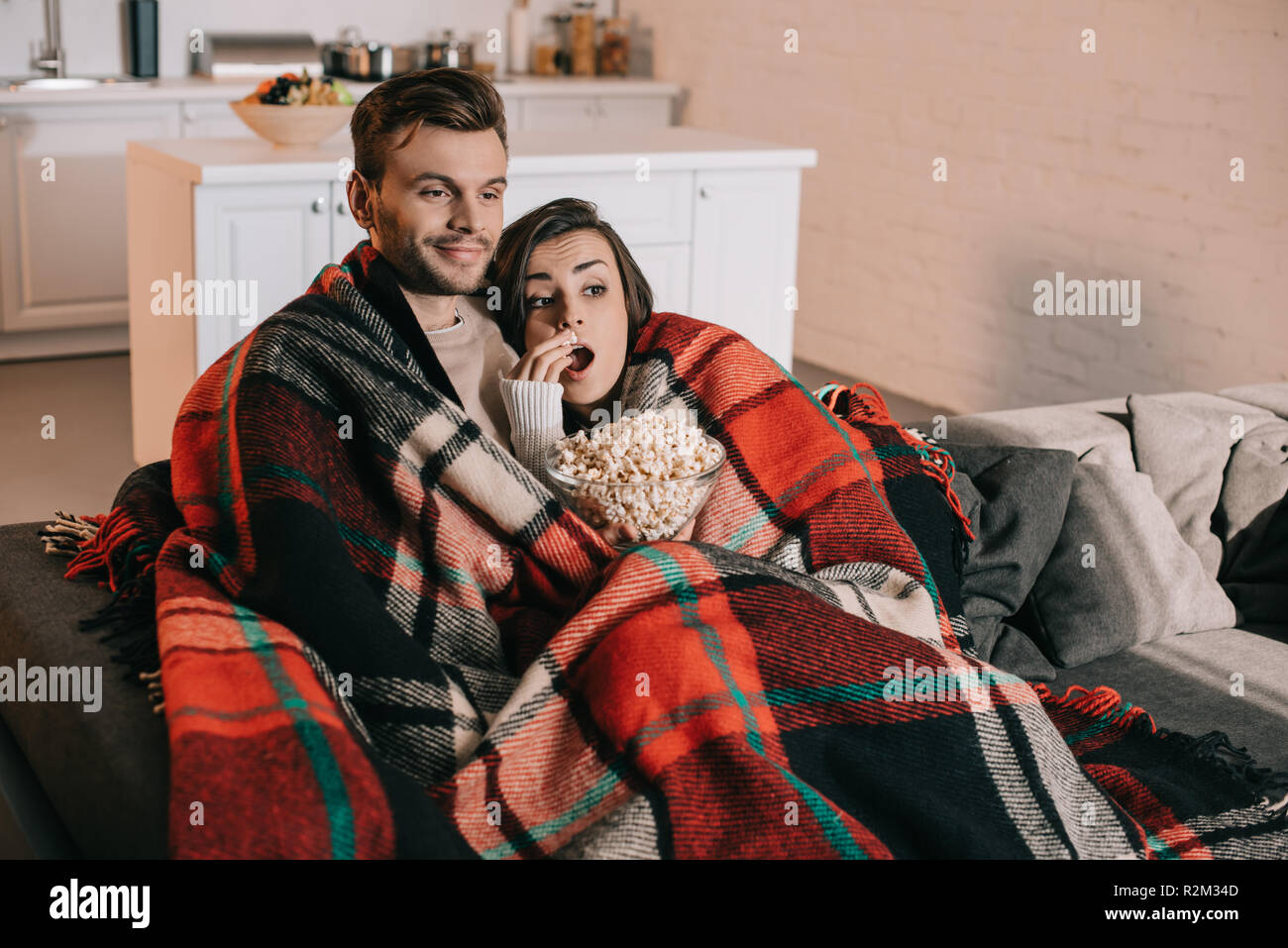 beautiful young couple watching movie with popcorn on couch and