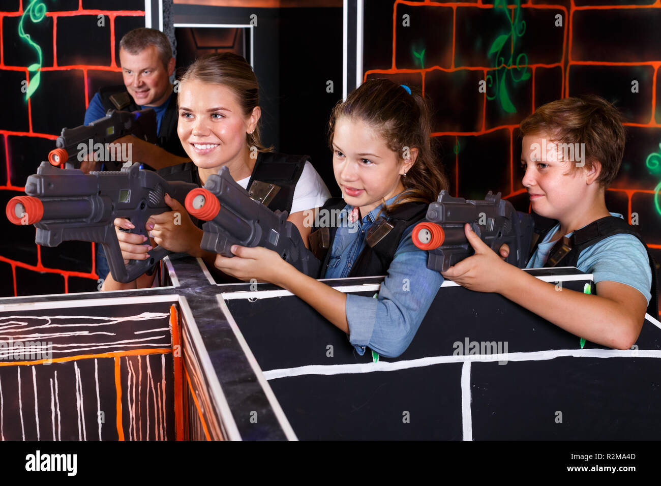 Smiling boy and girls aiming laser guns and playing laser tag game