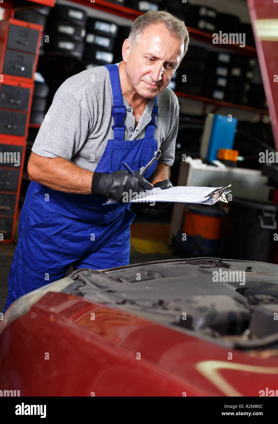 Skilled mature male mechanic taking notes in notebook about car repair
