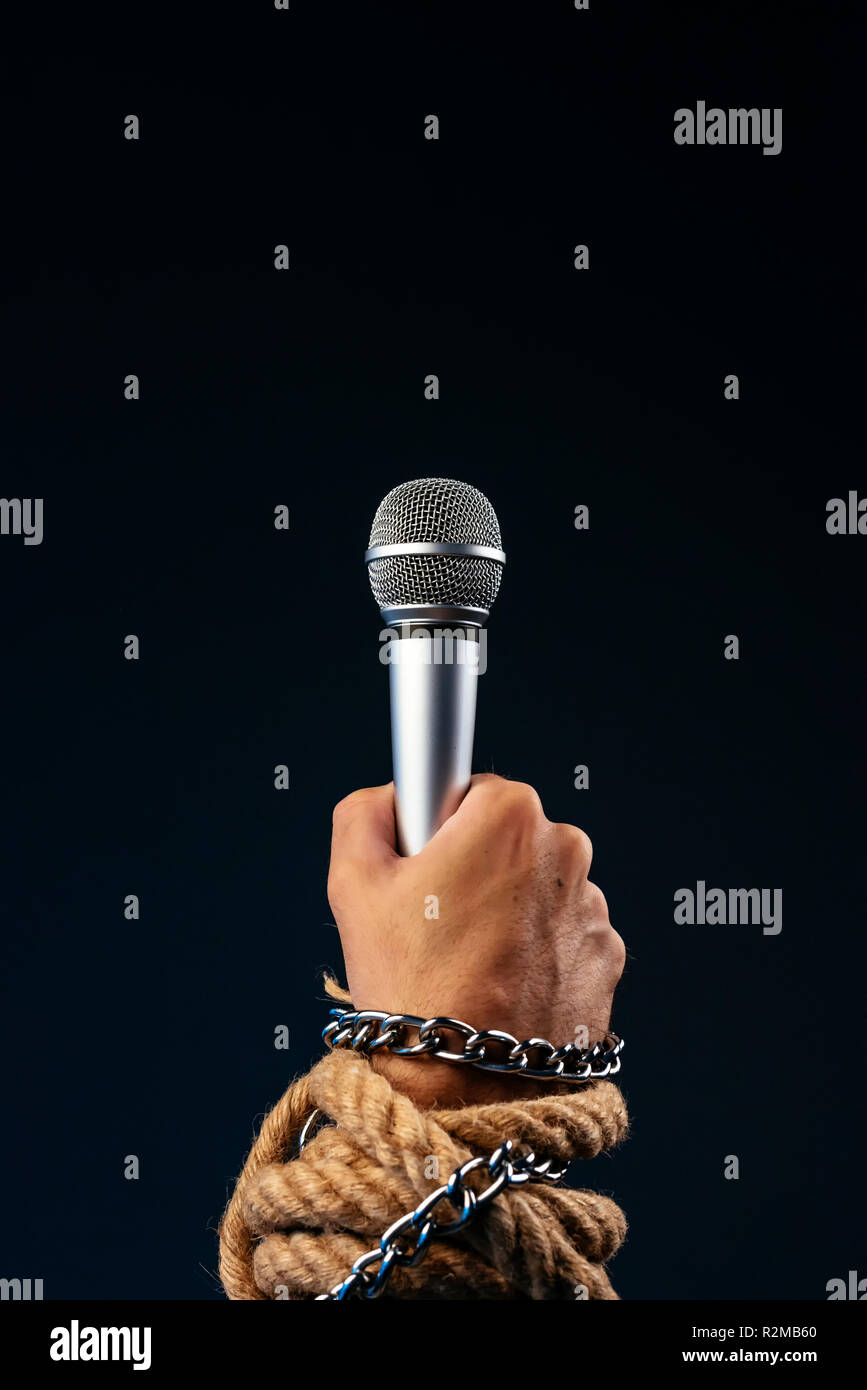 Freedom of the press and journalism, conceptual image with microphone in male hand tied with chains and ropes, low key image Stock Photo
