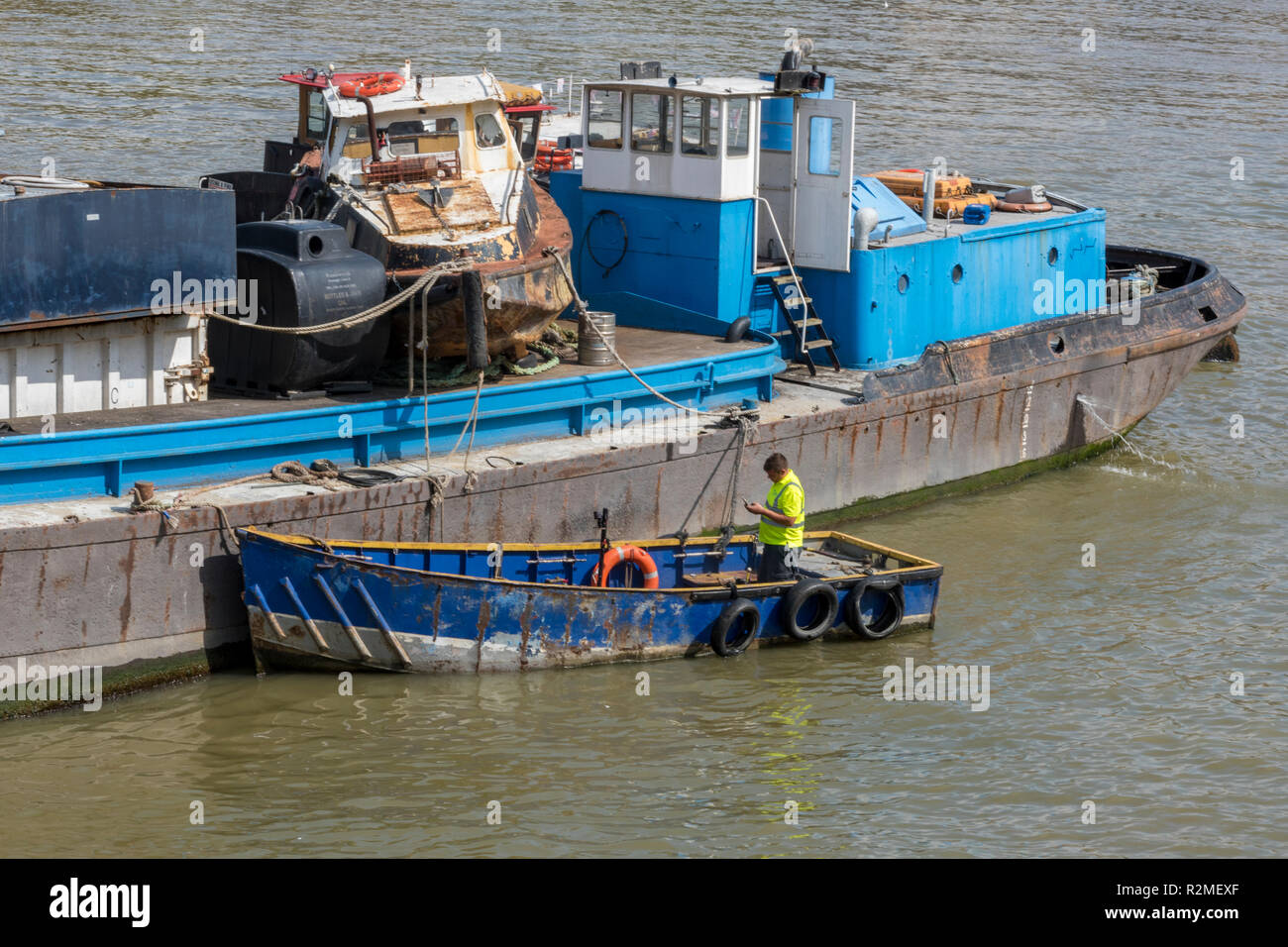 a man working on an old rusty boat on the river thames. thames working riverboat with man in