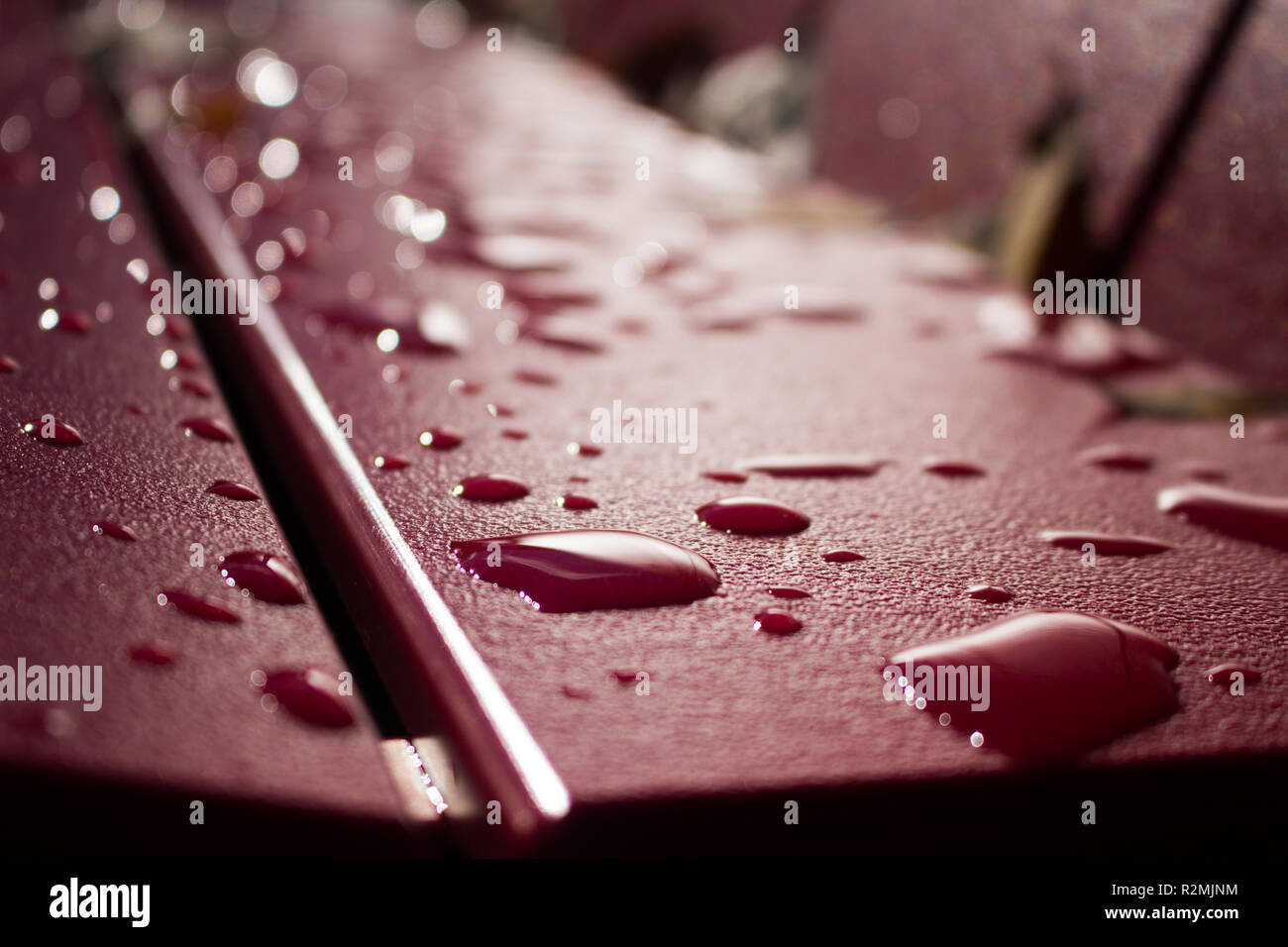 Closeup of water / rain / dew droplets on red park bench Stock Photo
