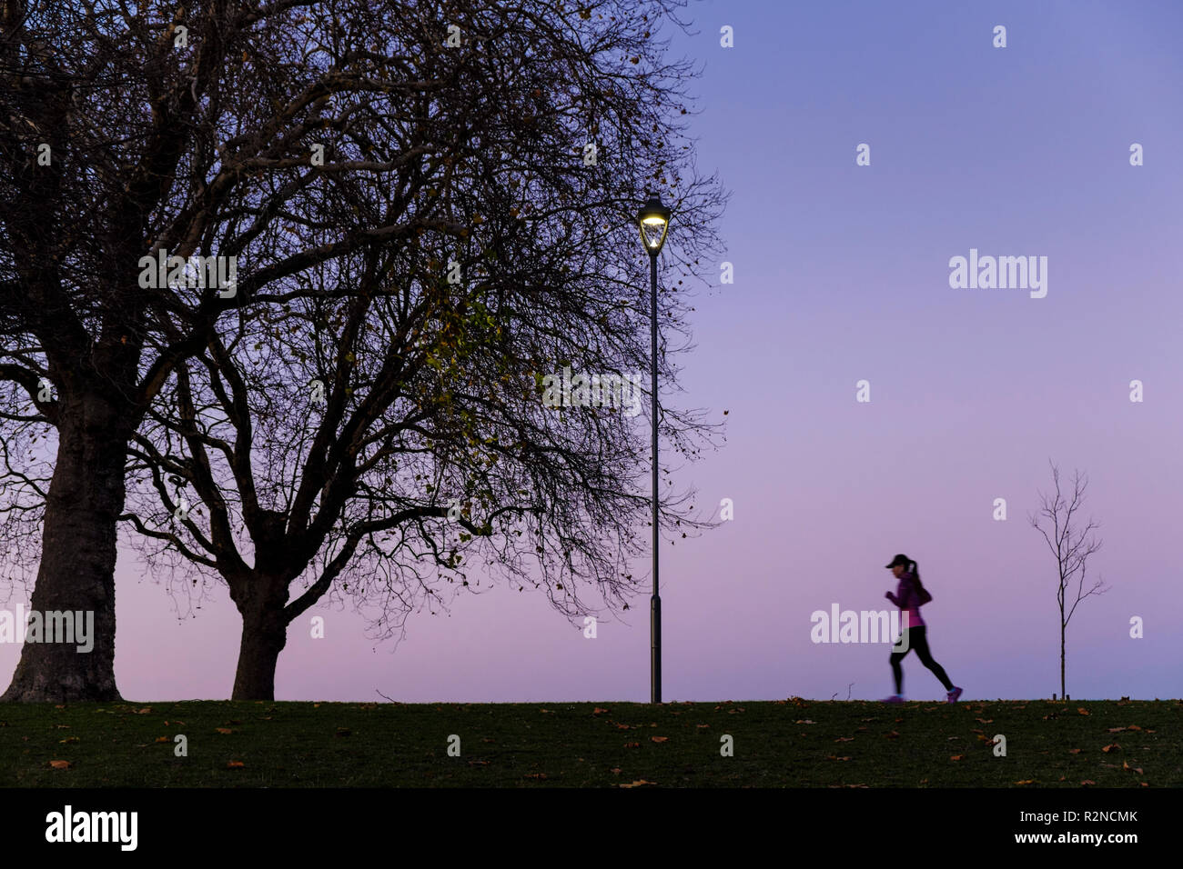 Person training. Woman running or jogging in a park at night, Nottingham, England, UK Stock Photo