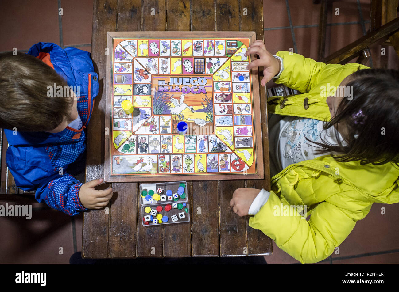 Little brothers playing Game of the Goose over wooden vintage table. Overhead view. Traditional board game Stock Photo