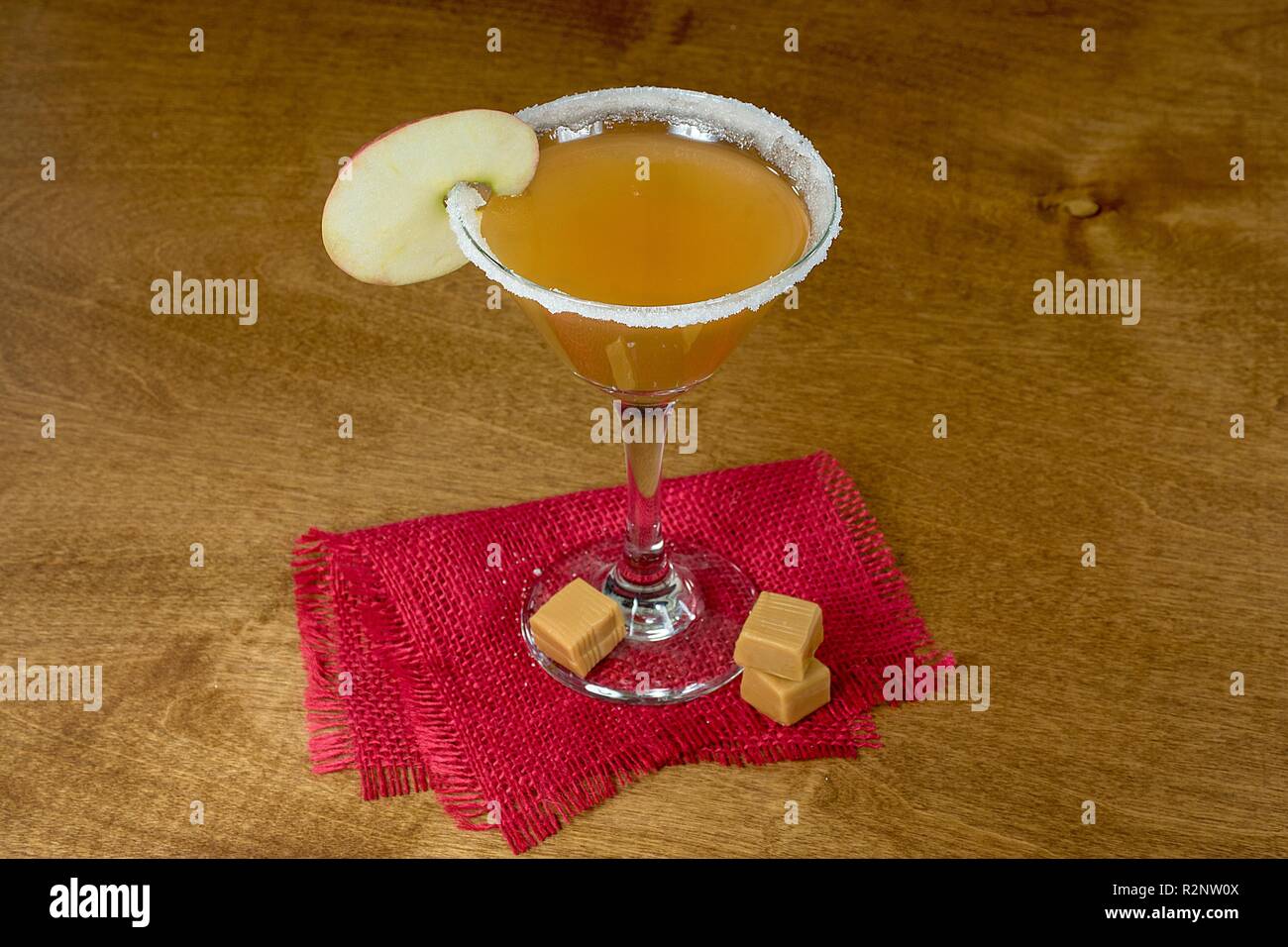 apple slice garnish on sugar rim martini cocktail glass with caramel candy and red burlap Stock Photo