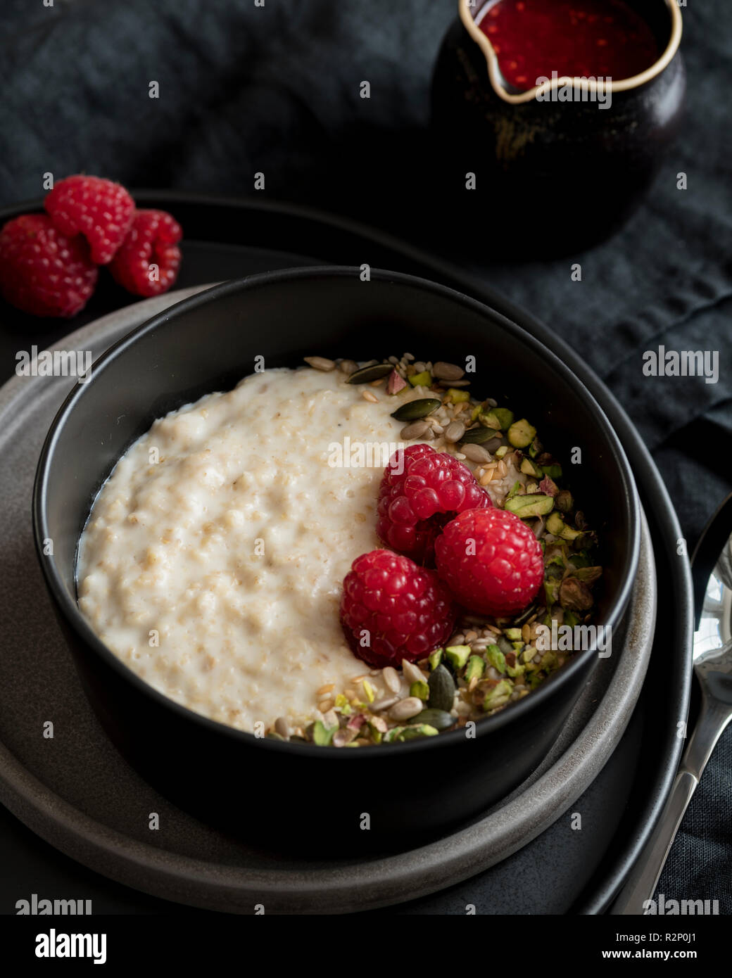 Porridge in dark bowl with nuts and soft fruit and fruit sauce Stock Photo