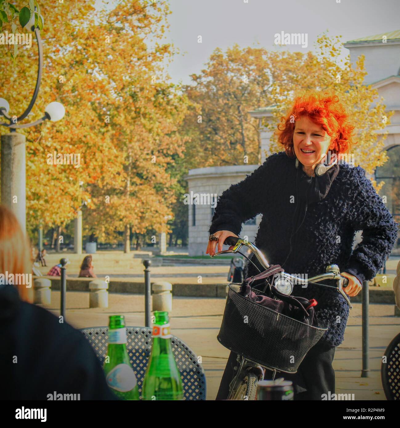 orange hair woman arrives with its bike to a restaurant at Sempione avenue, Milan, Italy Stock Photo