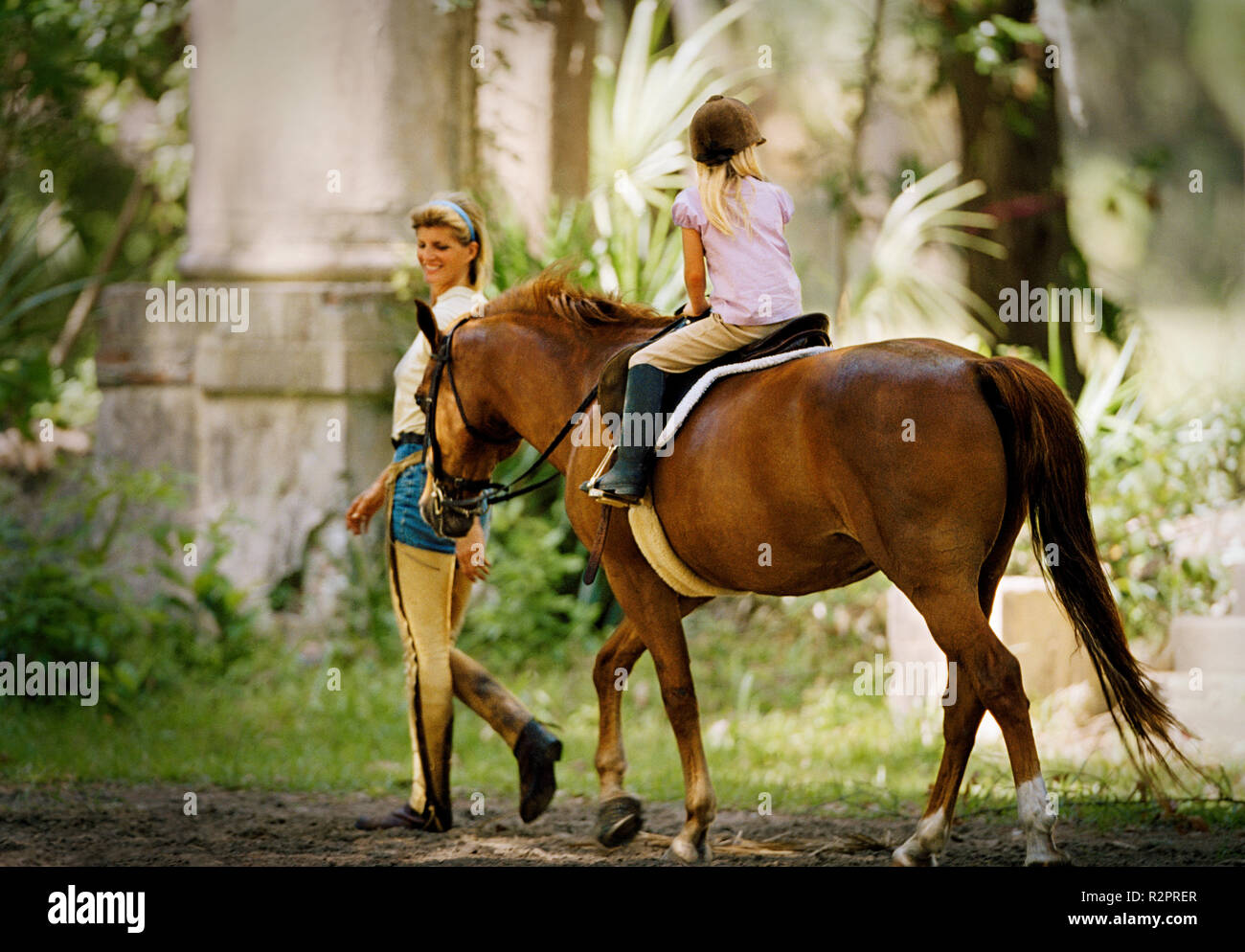 Mother walking alongside her daughter on horseback Stock Photo