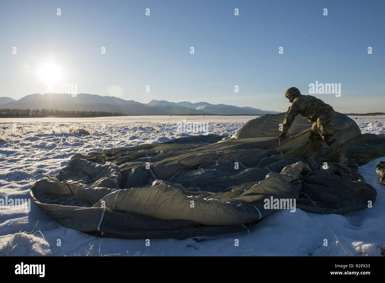 An Army paratrooper assigned to the 4th Infantry Brigade Combat Team (Airborne), 25th Infantry Division, U.S. Army Alaska, recovers his parachute after jumping from a CH-47 Chinook helicopter at Joint Base Elmendorf-Richardson, Alaska, Nov. 1, 2018. The Soldiers of 4/25 belong to the only American airborne brigade in the Pacific and are trained to execute airborne maneuvers in extreme cold weather and high altitude environments in support of combat, partnership and disaster relief operations. Army aviators from B Company, 1st Battalion, 52nd Aviation Regiment out of Fort Wainwright, operated C Stock Photo