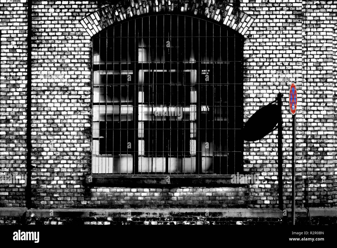 Closed industrial estate, 'No stopping' sign casting shadow on brick wall of old factory building, barred windows Stock Photo