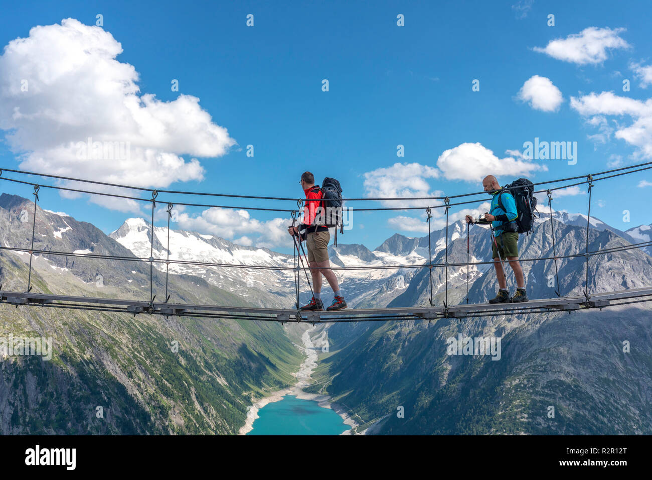 Two hikers on the tibetan bridge near Olperer hut with Schlegeis Stausee on the background, Zillertal Alps, Tyrol, Schwaz district, Austria. Stock Photo