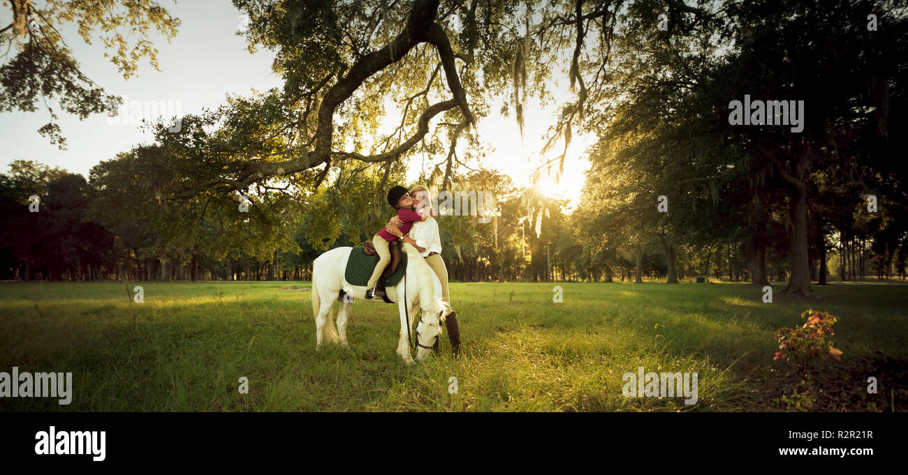 Mother hugging her daughter while she sits upon her horse. Stock Photo