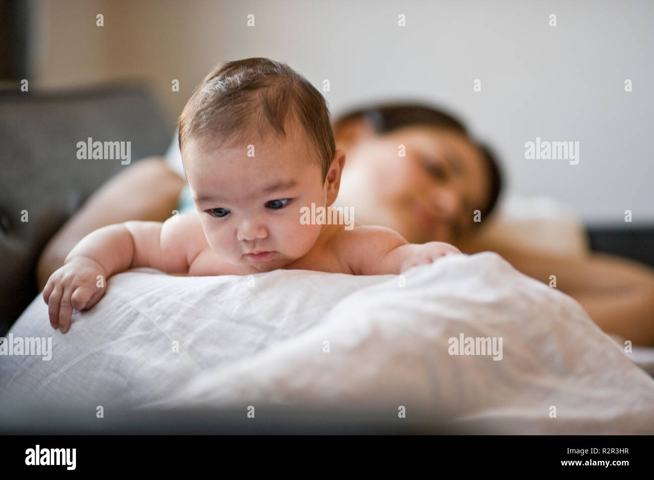 Cute baby lying with his tired mother on a sofa. Stock Photo