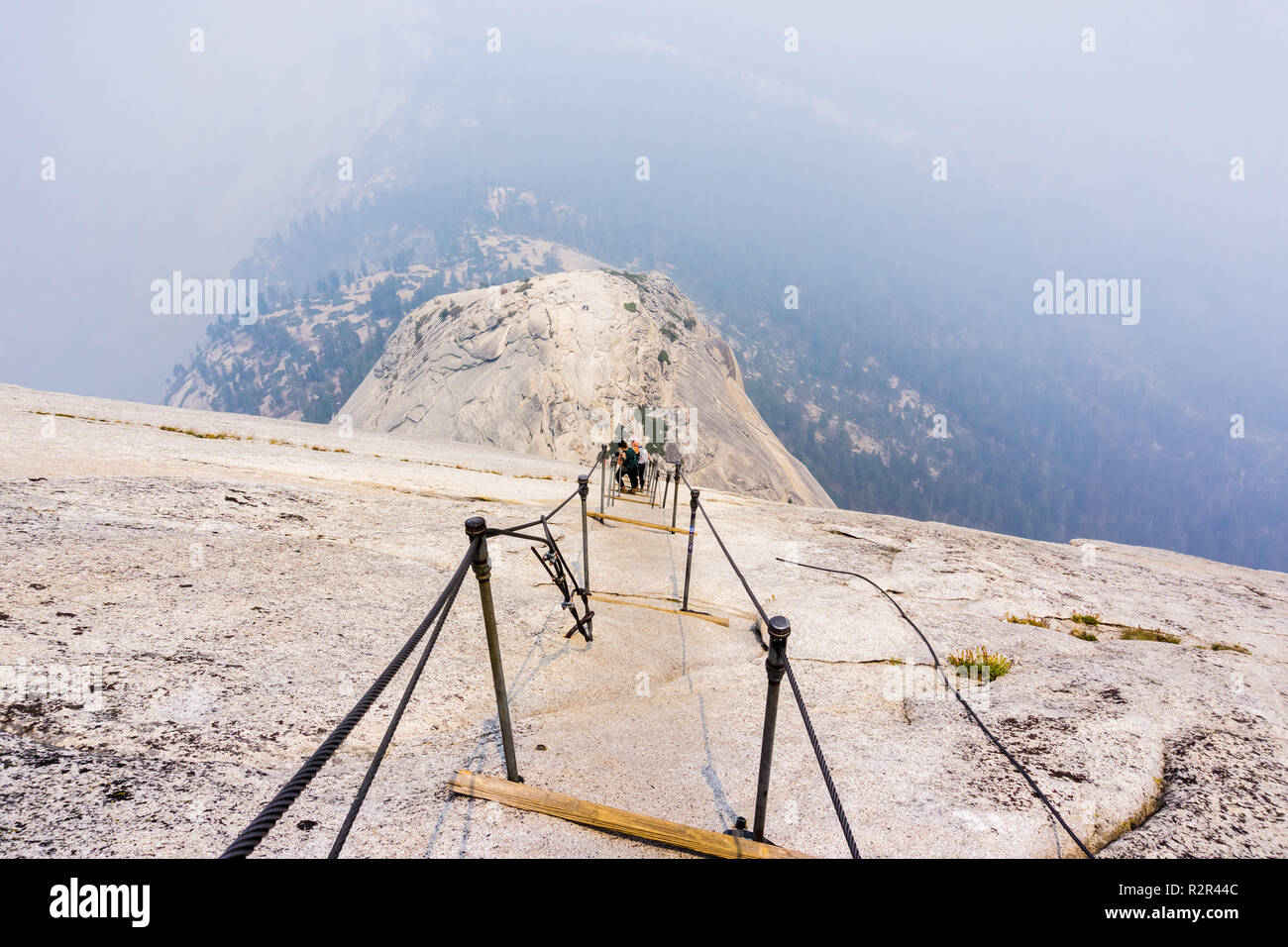 Looking down on the Half Dome cables on a summer day; smoke covering the sub dome and the valley beyond; Yosemite National Park, California Stock Photo