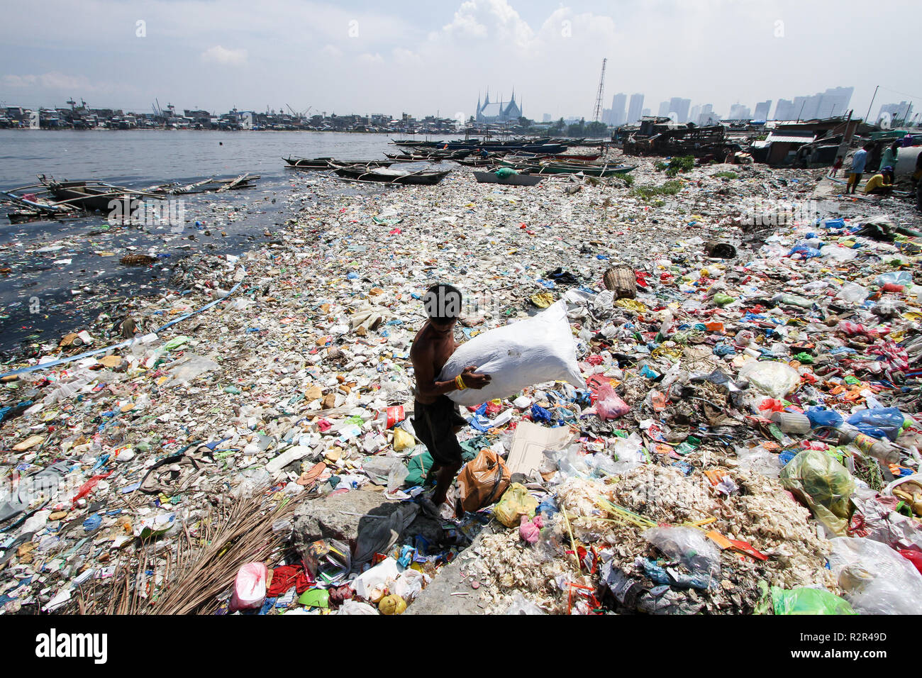 A scavenger collects recyclable waste materials from the sea of garbage that makes up a portion of the polluted bayside in Manila, Philippines. Stock Photo