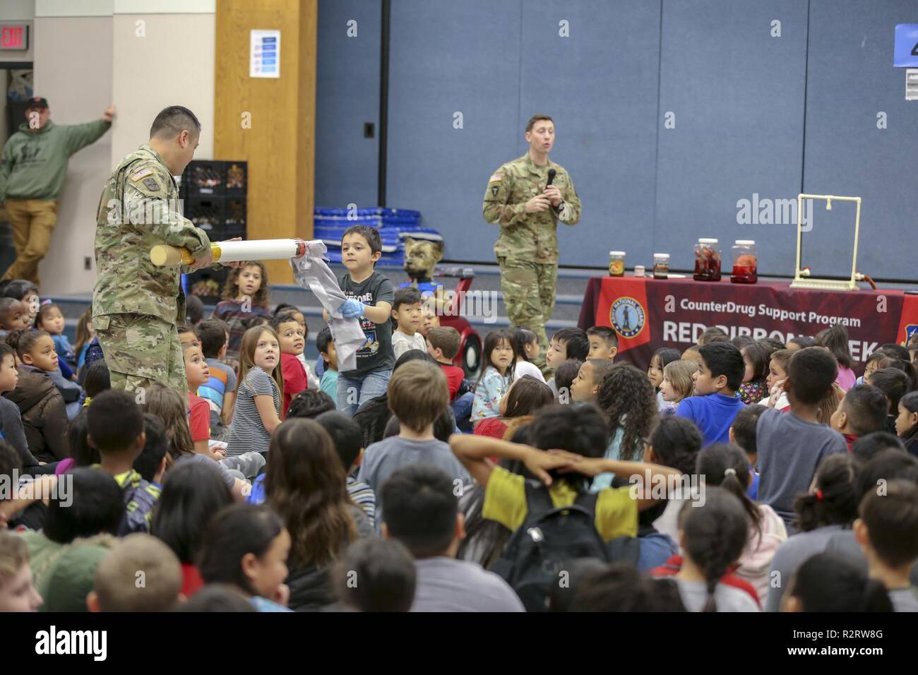 Sgt. 1st Class Oliver Meza, Army National Guard drug testing coordinator, and his student assistant display a 5-foot fake cigarette with a list of up to 7,000 chemicals in cigarettes that are harmful during a Red Ribbon Week drug free celebration at Muldoon Elementary School, October 29, 2018.  The event brought multiple law enforcement agencies together to promote a healthy and drug-free lifestyle by greeting students upon arrival at school, static displays of military and police vehicles, and a drug free message. Stock Photo