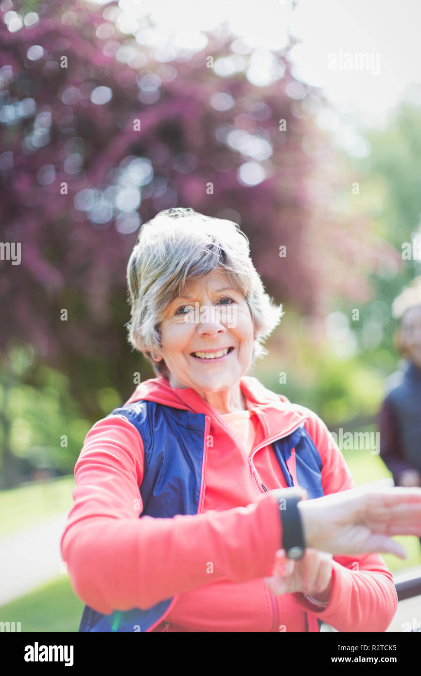 Portrait smiling, confident active senior woman checking smart watch in park Stock Photo