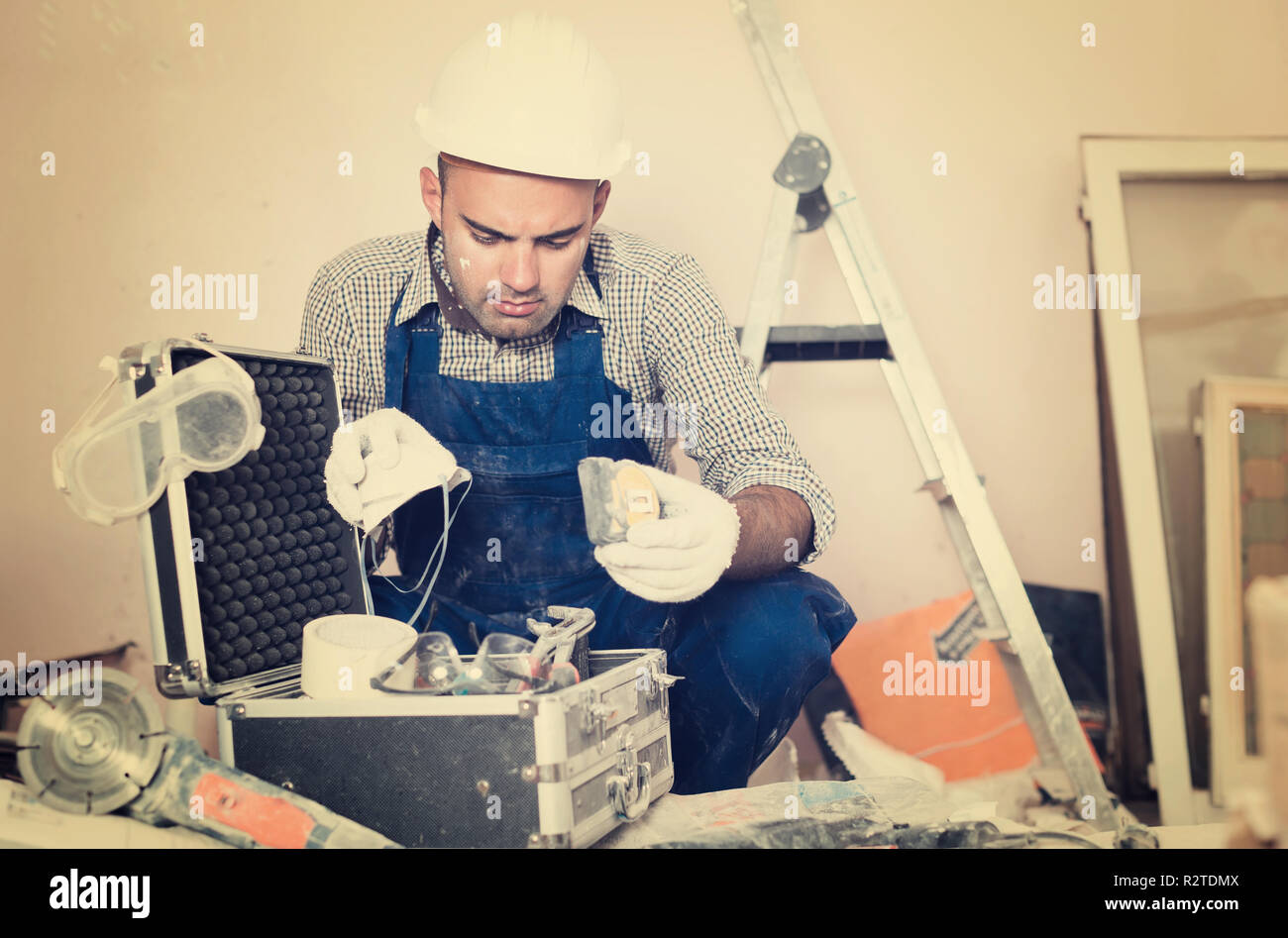 worker builder is carefully looking  tools for repair in toolbox Stock Photo