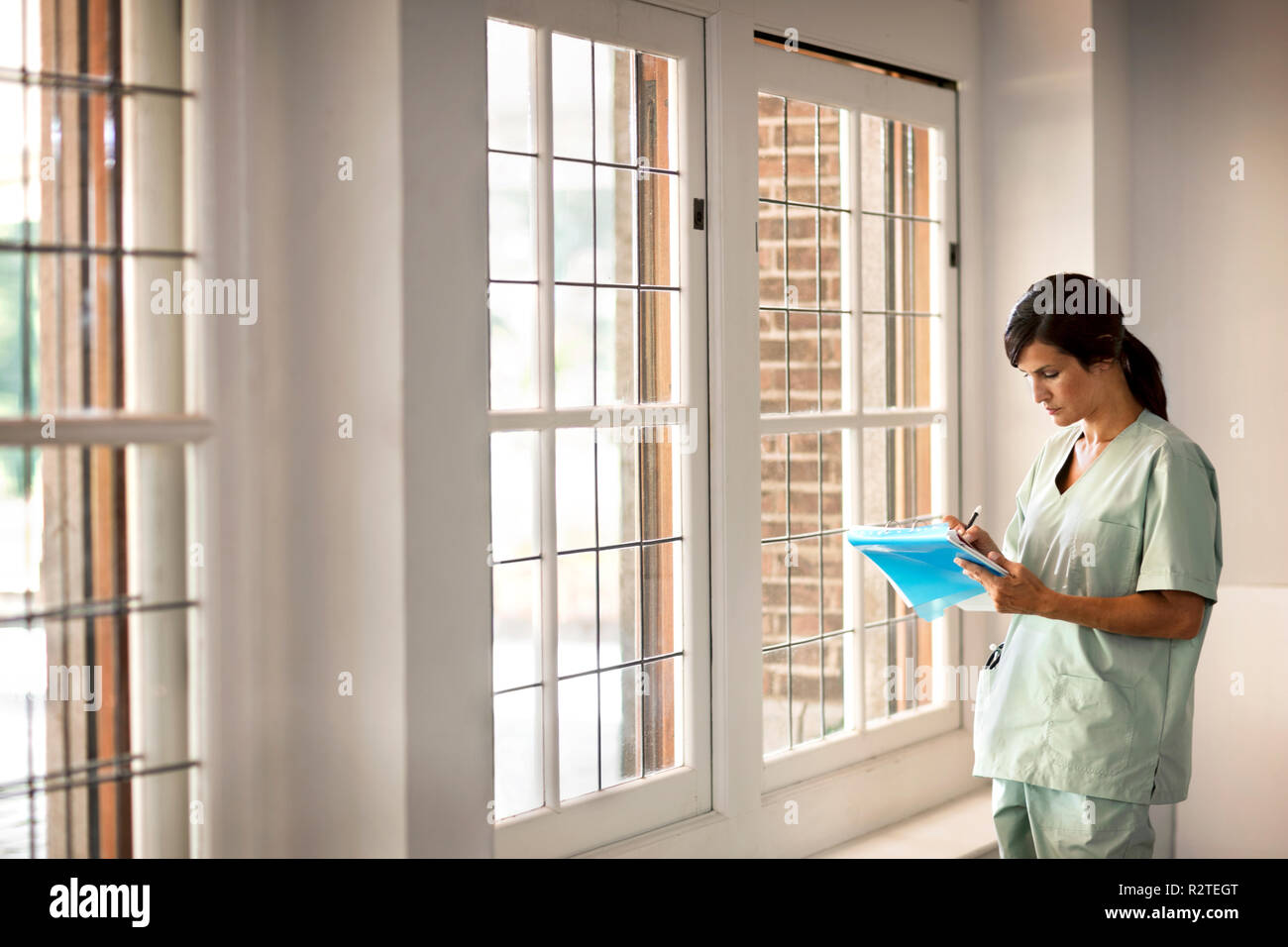 Female doctor in scrubs making notes in someones file. Stock Photo
