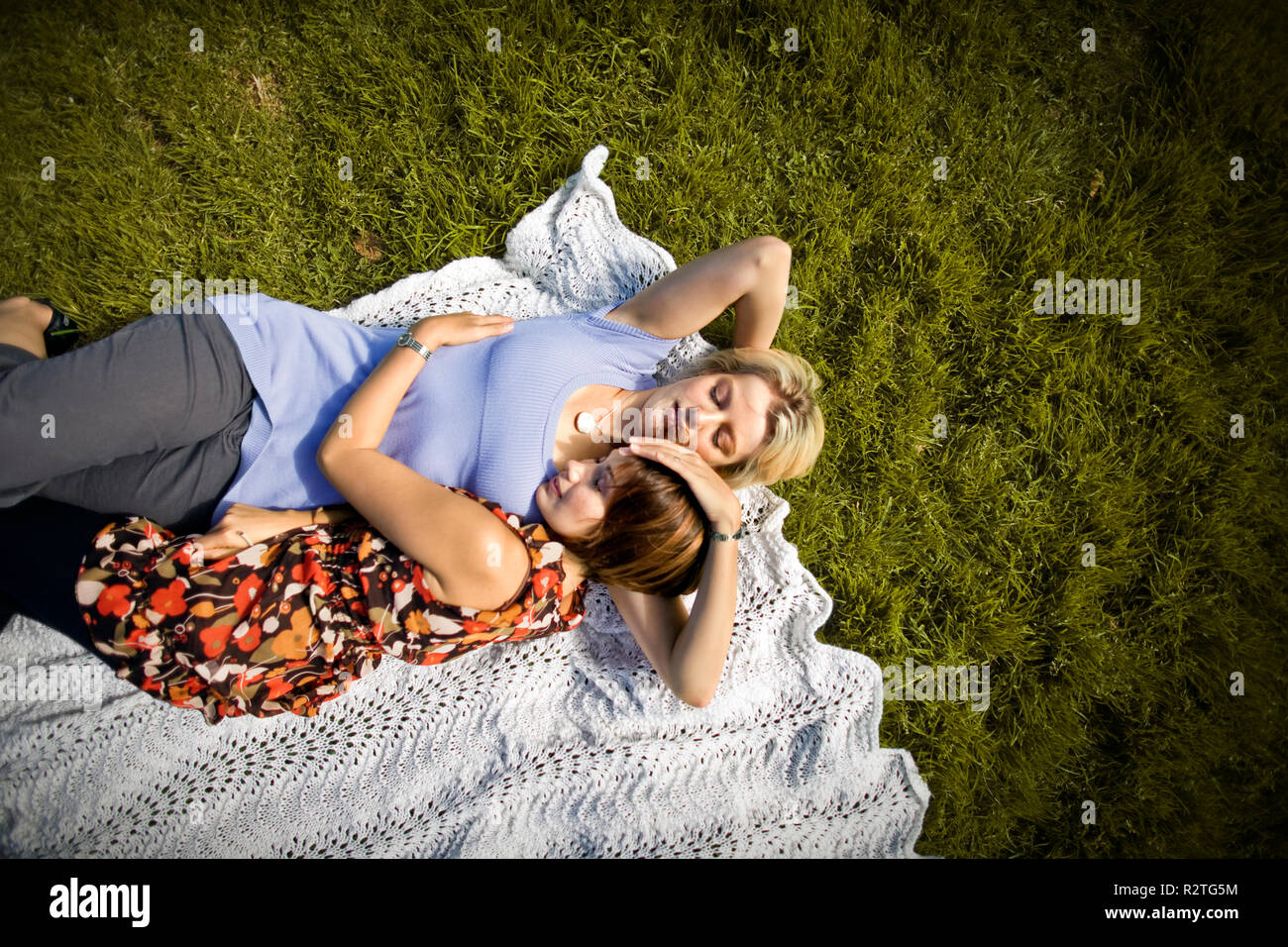 Two mid-adult woman lying on a blanket on the grass hugging. Stock Photo