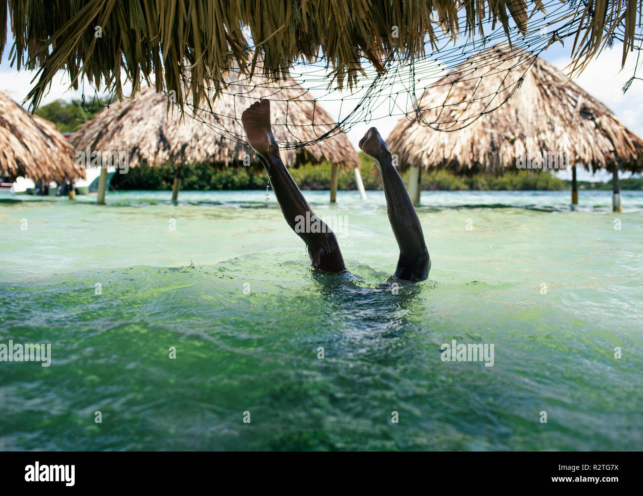 Caribbean boy doing a handstand. Pristine water & mangrove beach pavilions (cabanas) on Playa Cholón, Colombia. Travel & holiday concept. Oct 2018 Stock Photo