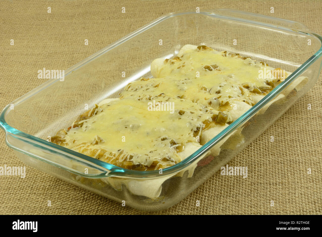 Baked chicken and bean enchildas smothered in salsa verde and cheese in glass baking dish Stock Photo