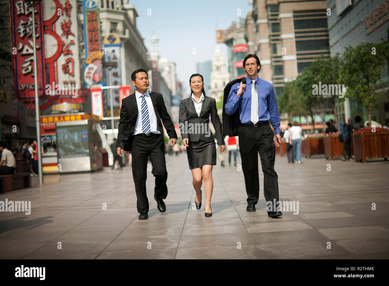 Three business colleagues walking down a busy street while talking. Stock Photo
