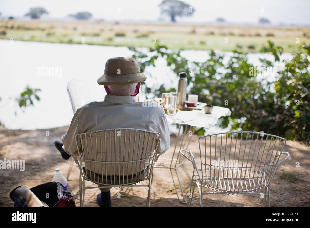 Senior man reading on a chair under a tree beside a lake. Stock Photo