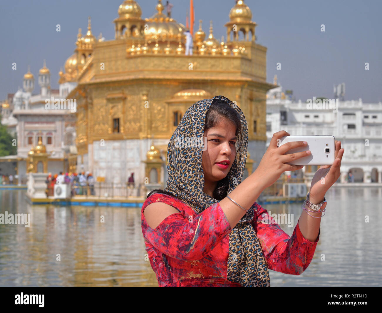 young indian beauty with dupatta takes a selfie with her smartphone in front of the golden temple R2TN1D