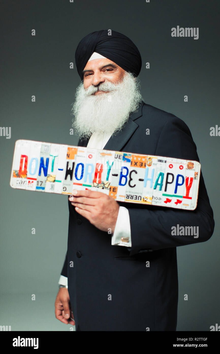 Portrait smiling, well-dressed senior man in turban holding  Dont Worry Be Happy  license plates Stock Photo