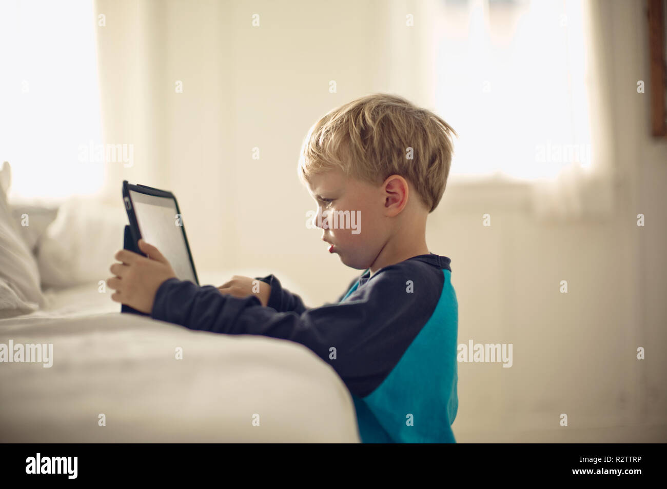 Young boy looking serious as he plays with a portable information device. Stock Photo