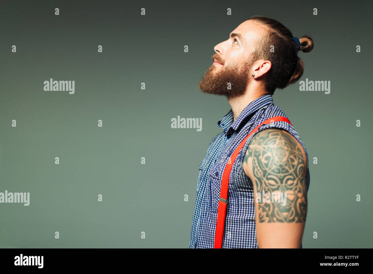 Curious hipster man with beard and shoulder tattoo looking up Stock Photo