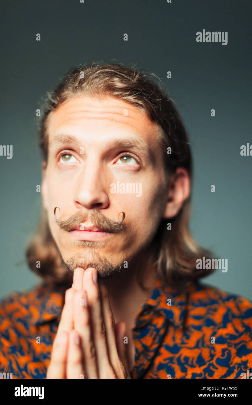 Portrait hopeful young man with handlebar mustache praying Stock Photo