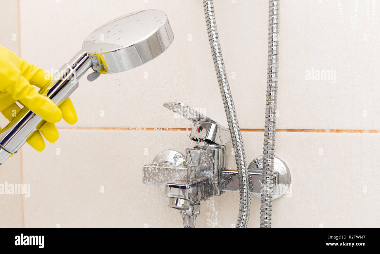 Person wearing yellow sanitary gloves rinsing tap with water from shower Stock Photo